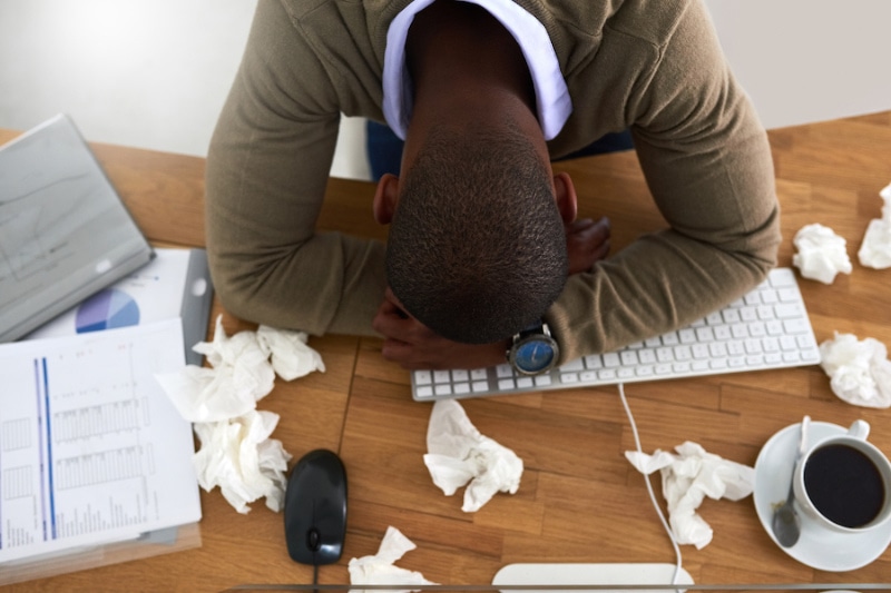 Air Conditioning & Allergies - High angle shot of a young businessman feeling ill at his work desk